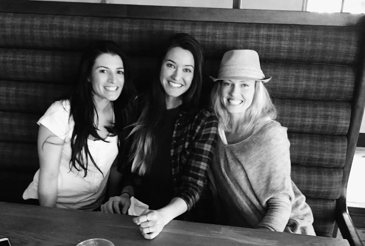 Three women squeezed into a restaurant booth, all laughing at once
